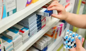 Ręka wybiera lek z półki aptecznej. W dłoni trzyma opakowanie z kapsułkami. Klacid na co? Na infekcje bakteryjne.