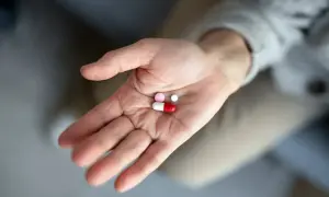 Dłoń trzyma kilka tabletek, w tym jedną czerwonobiałą kapsułkę, która może być antybiotykiem na zęba.