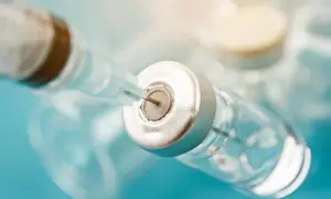 Igła strzykawki wbita w fiolkę z płynem, przygotowanie do podania szczepionki na wściekliznę.