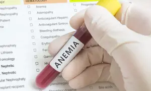 Ręka w rękawiczce trzyma probówkę z krwią z napisem "ANEMIA". Obok znajduje się lista badań, gdzie zaznaczono "Anemia", sugerując diagnostykę i poszukiwanie sposobów, jak leczyć anemię.