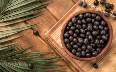Misternie ułożone owoce acai w drewnianej misce, otoczone liśćmi palmowymi. Zastanawiasz się acai co to? To egzotyczne jagody pełne zdrowia!