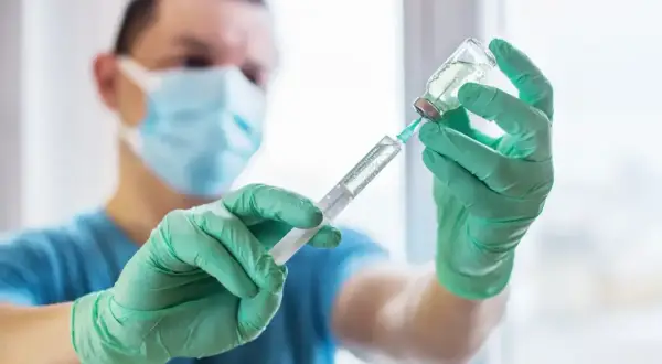 Medyk w masce i rękawiczkach przygotowuje zastrzyk. To ważny krok w kierunku szczepienia na tężec, chroniącego przed groźną chorobą.