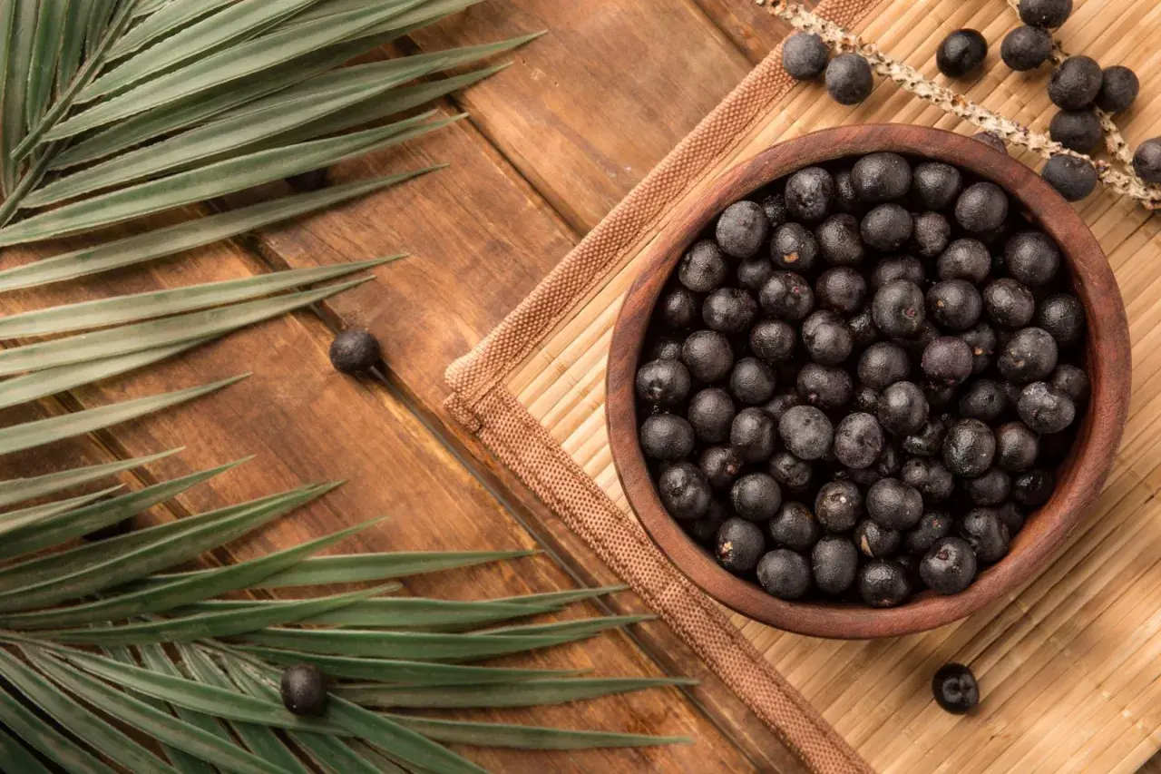 Misternie ułożone owoce acai w drewnianej misce, otoczone liśćmi palmowymi. Zastanawiasz się acai co to? To egzotyczne jagody pełne zdrowia!